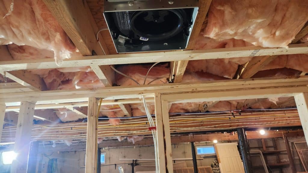 Bathroom exhaust fan housing installed between basement ceiling joists