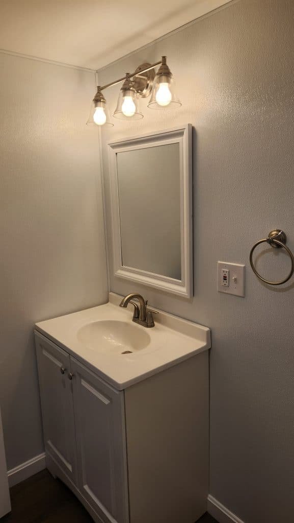 Finished basement bathroom vanity with three-light bar and GFCI outlet