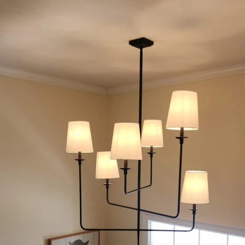 Six-light chandelier with white shades installed in a two-story entryway